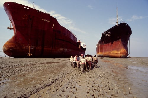 due grandi navi container in secca sul fango, in mezzo a loro dei marinai camminano sulla sabbia