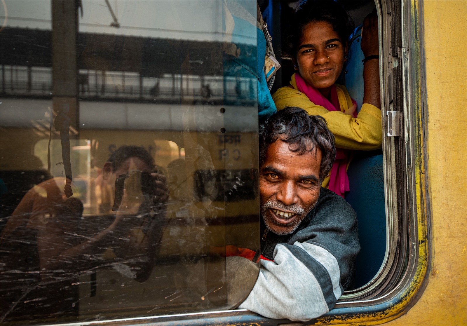 Due uomini indiani sorridono alla fotocamera da dentro un vagone con un finestrino appena aperto
